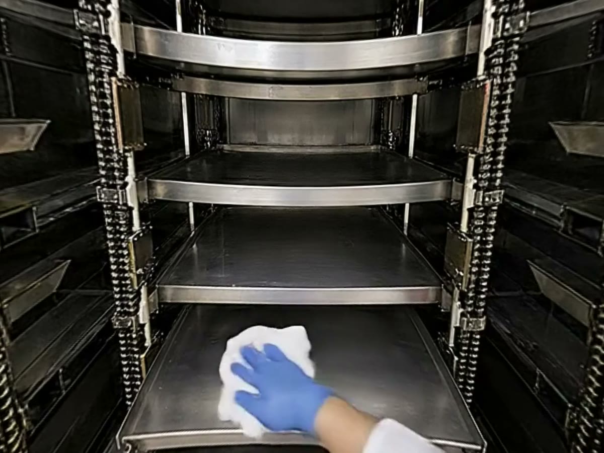 食品工場の機械の中で、自分の青い手袋の手が布で棚を拭いている当事者目線の映像。実際の教材の一場面